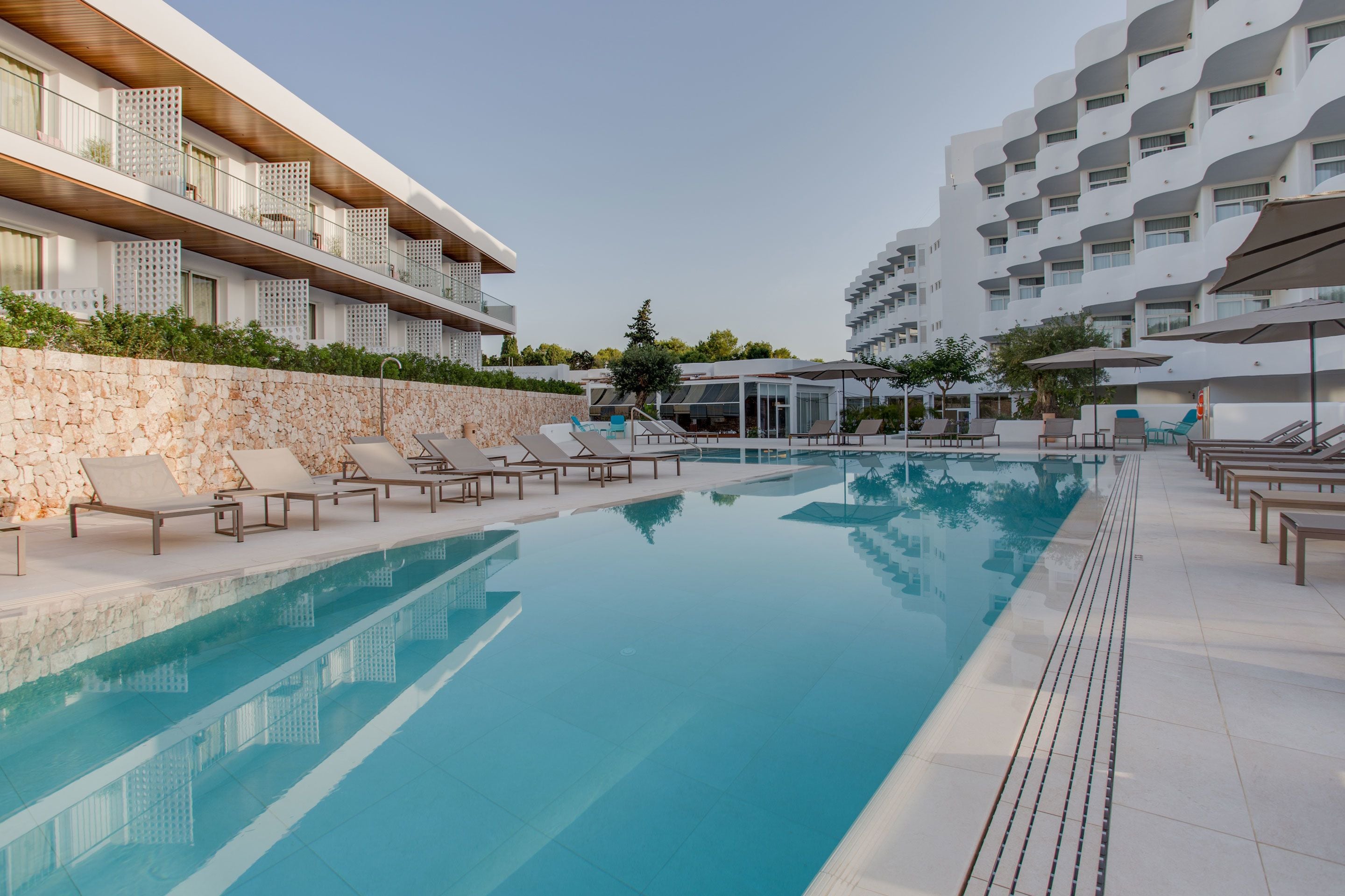A modern hotel with a swimming pool, lounge chairs, and a stone wall.