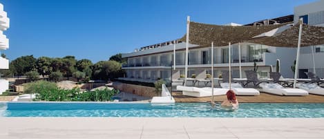 A modern pool area with a clear blue sky, a pool, lounge chairs, and a building with balconies.