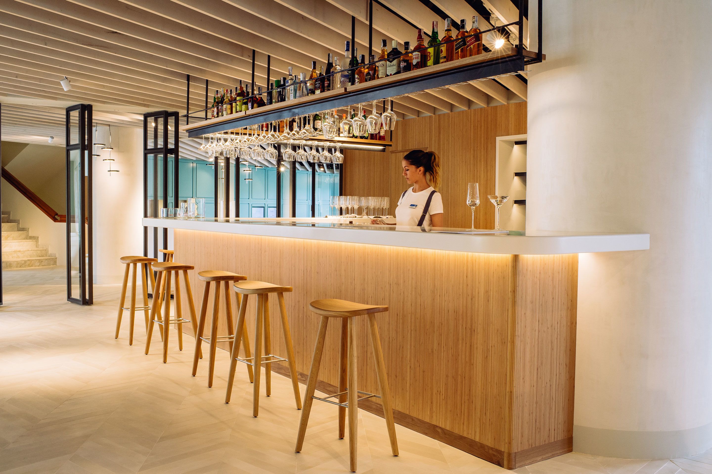 Een moderne bar met houten krukken, een bargedeelte en diverse flessen en glazen.