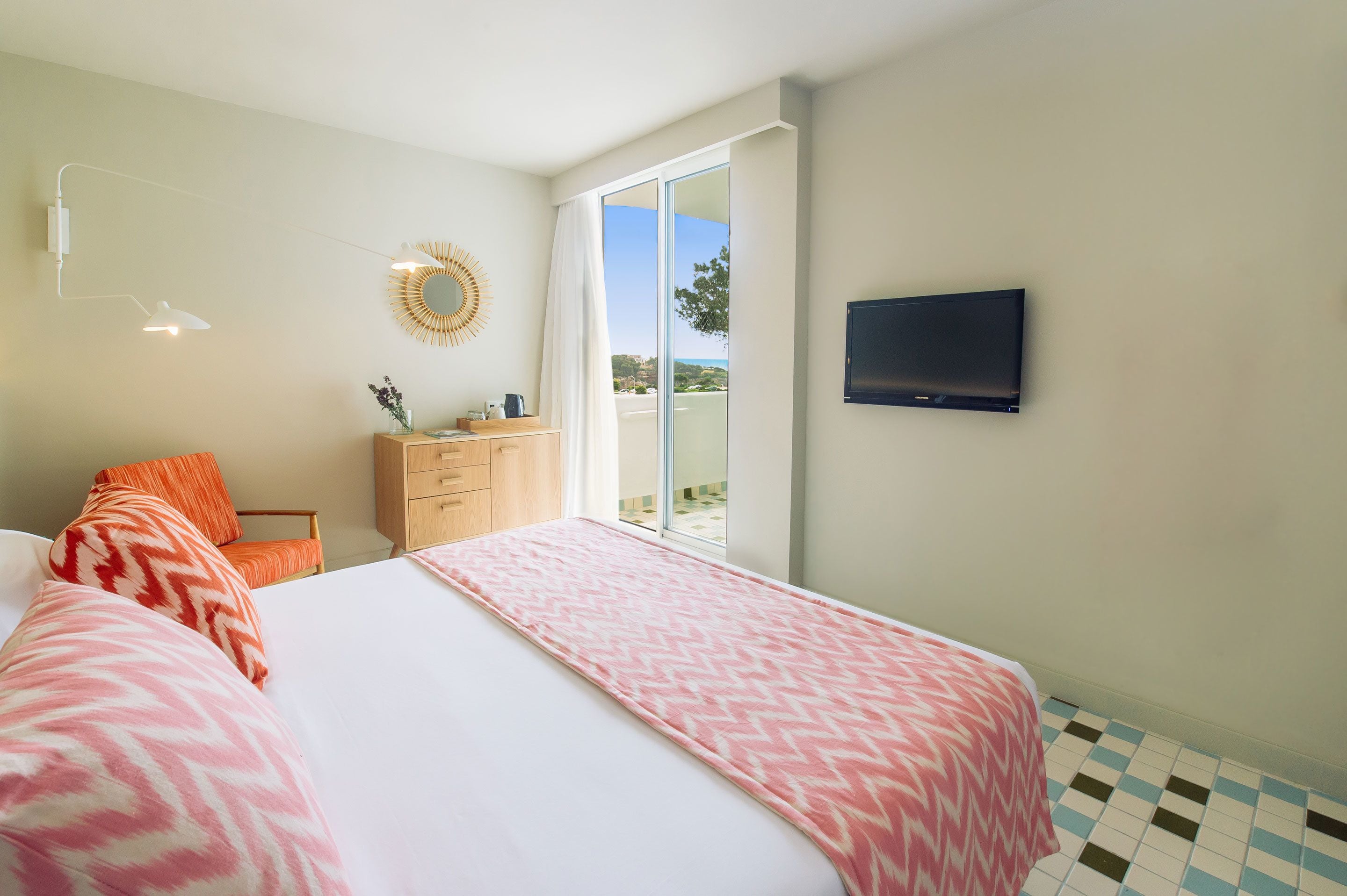 A hotel room with a bed, a TV, a dresser, a chair, and a view of the outdoors.
