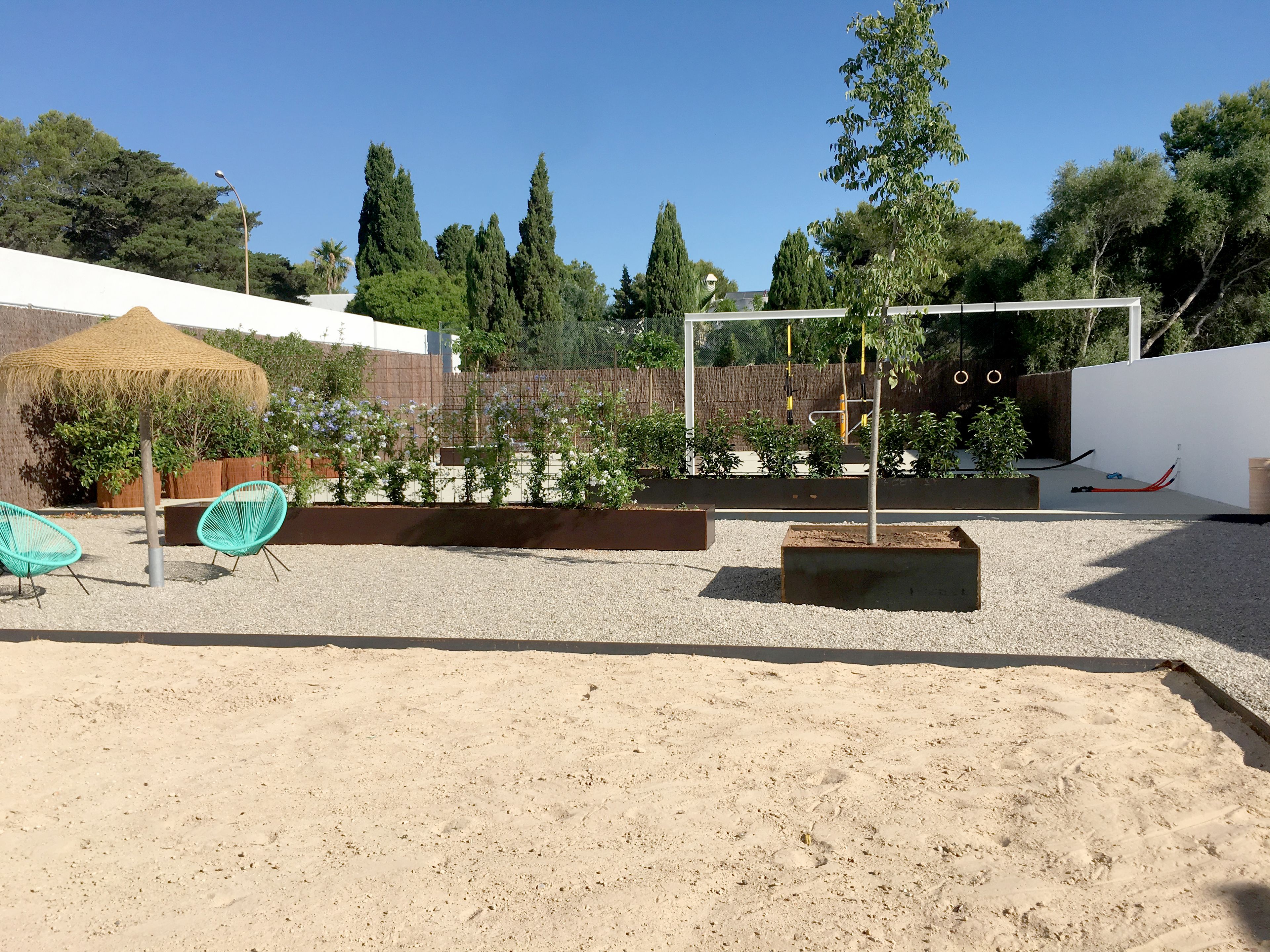 Ein Garten mit einer Pergola, einer Sitzgelegenheit und verschiedenen Pflanzen.