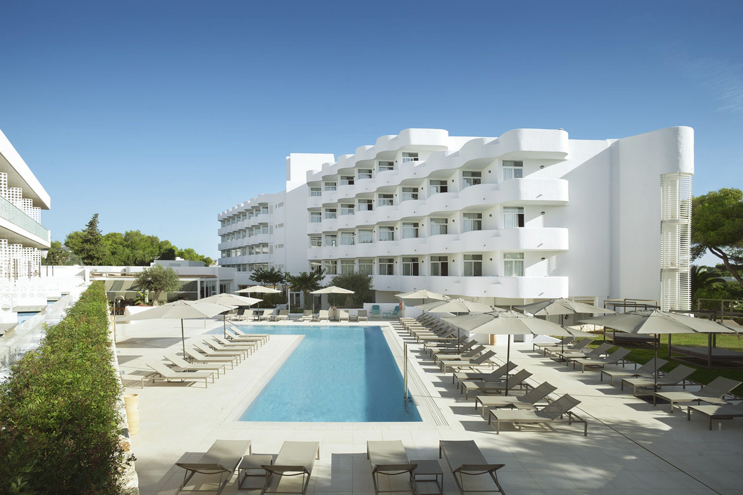 A modern hotel with a swimming pool, sun loungers, and umbrellas.