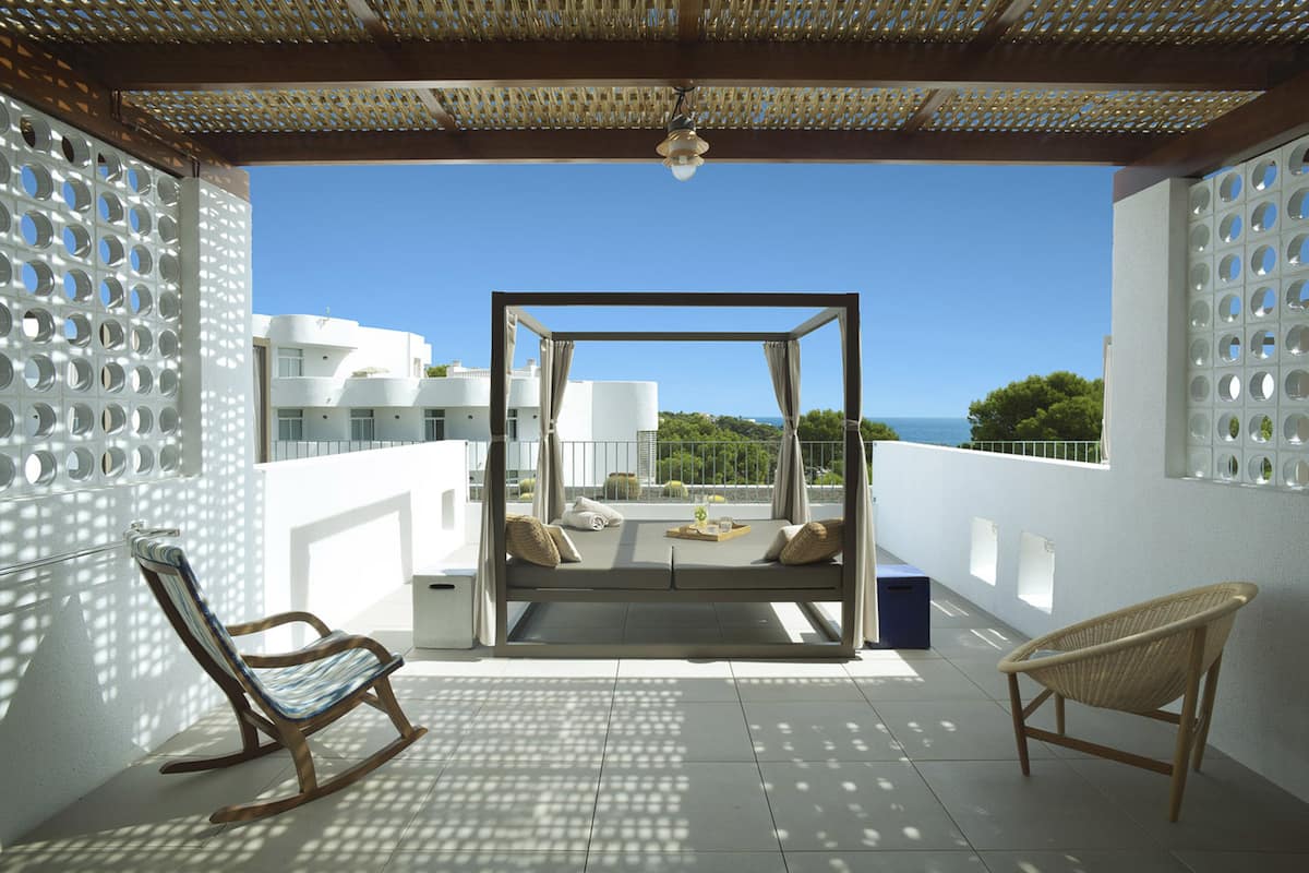 Un balcón con vista al mar, una silla colgante, una mecedora y una silla de mimbre.