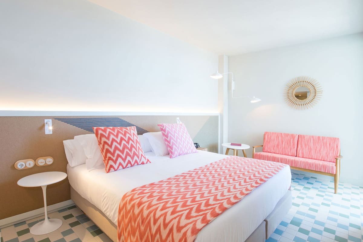 Habitación de hotel con cama, una mesita redonda, sofá y una lámpara fijada en la pared.