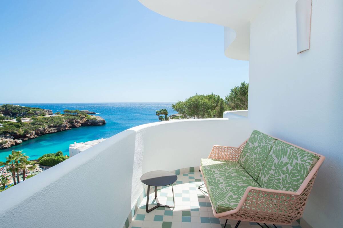 Un balcón con vista al mar, una silla de mimbre y una pequeña mesa.