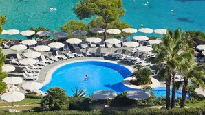 Ein Poolbereich mit Liegestühlen und Sonnenschirmen, umgeben von Bäumen und Blick auf das Meer.