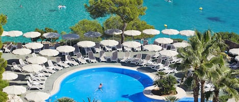 A pool area with lounge chairs and umbrellas, surrounded by trees and a view of the sea.