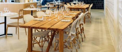 A restaurant with wooden tables and striped chairs, a tiled backsplash, and pendant lighting.