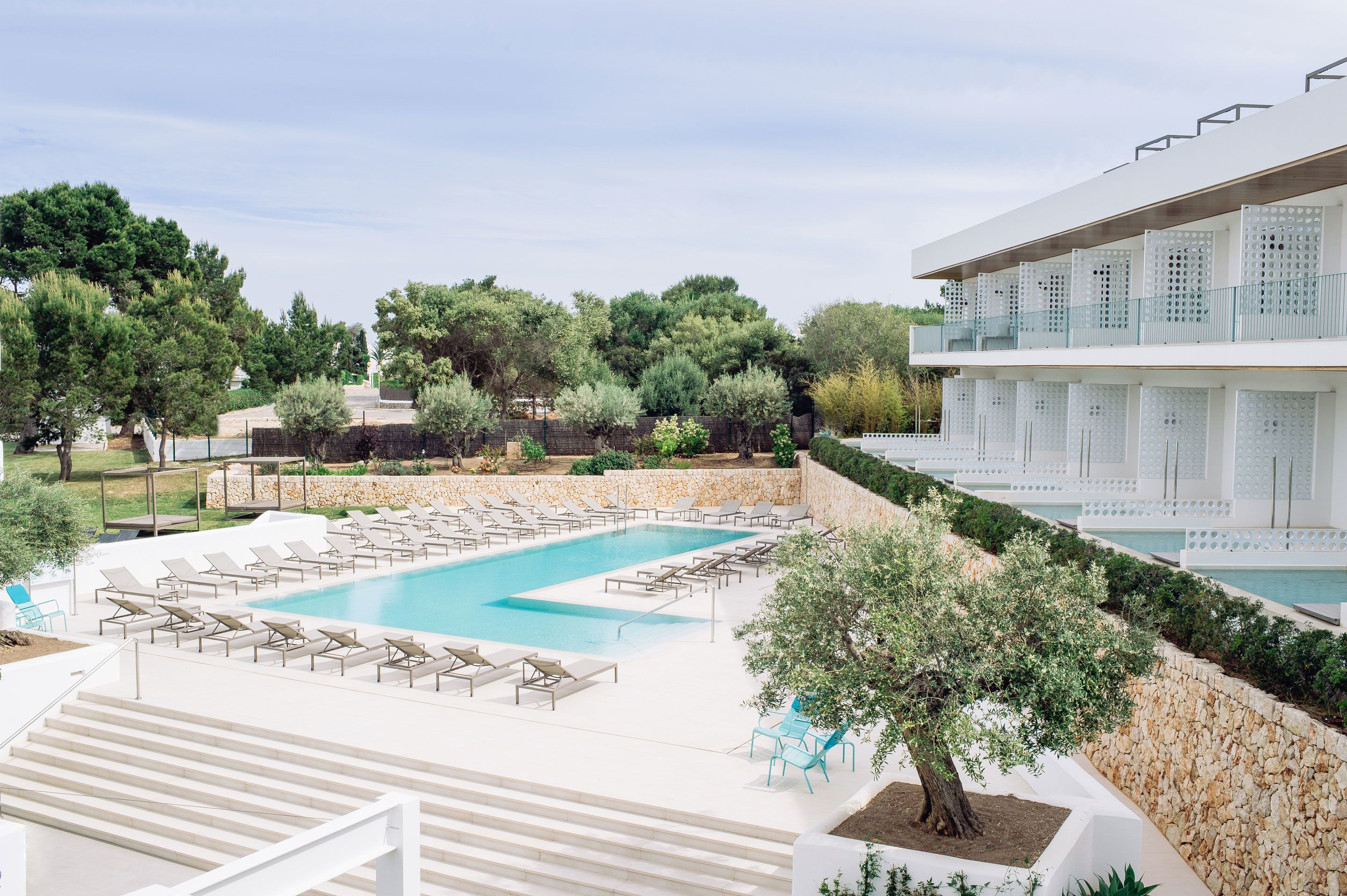 A pool area with lounge chairs, a stone wall, and a building with balconies.