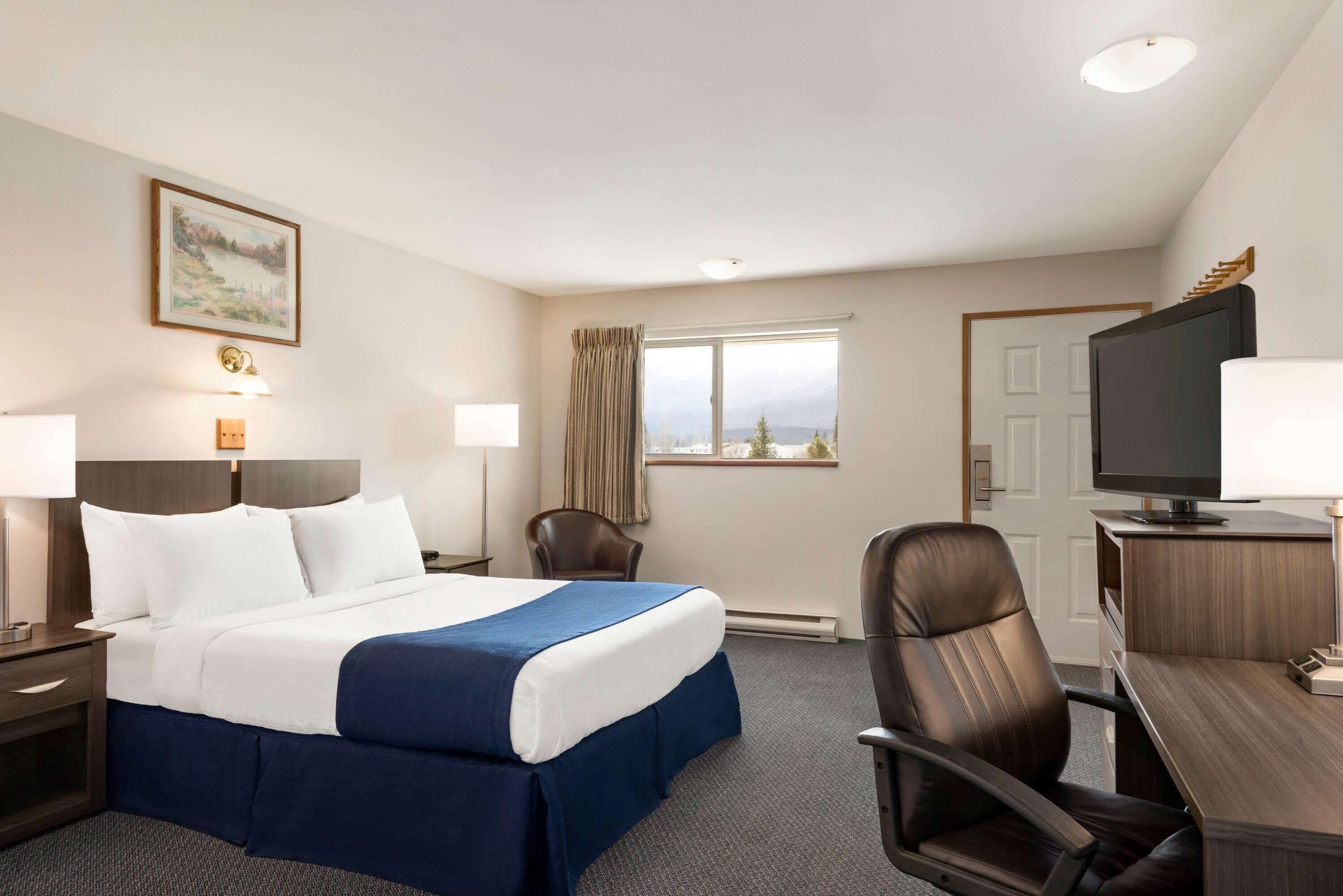 A hotel room with a bed, a desk, a chair, a television, and a window with a view.