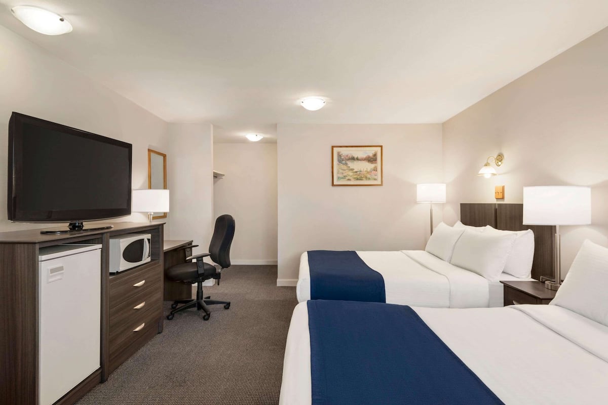 Ein Hotelzimmer mit zwei Betten, einem Schreibtisch mit Computer, einem Fernseher und einem kleinen Kühlschrank.