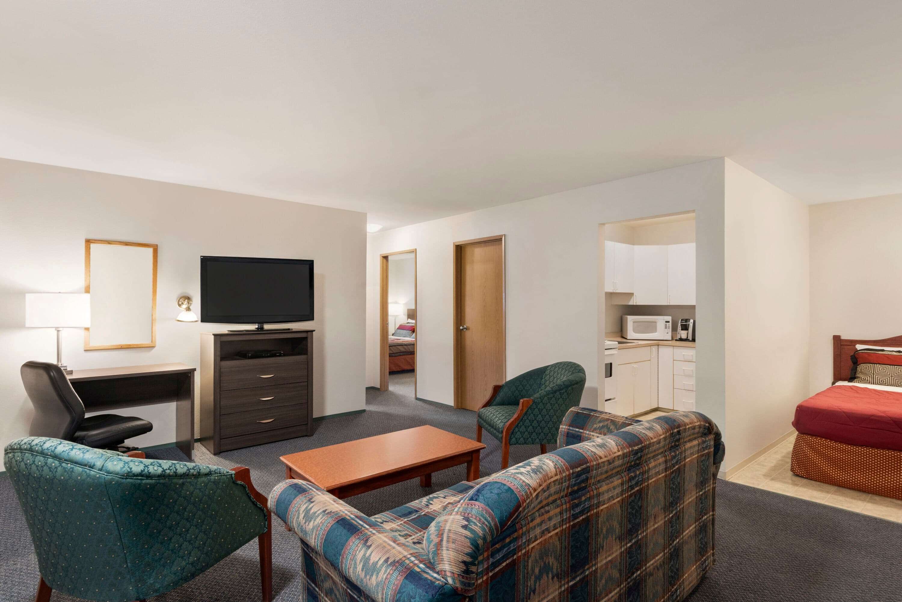 A hotel room with a TV, a desk, a sofa, a chair, and a bed.