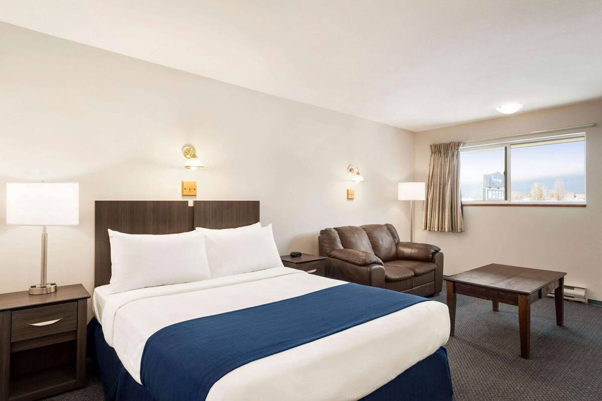 Ein Hotelzimmer mit Bett, Stuhl, Tisch und einem Fenster mit Blick.