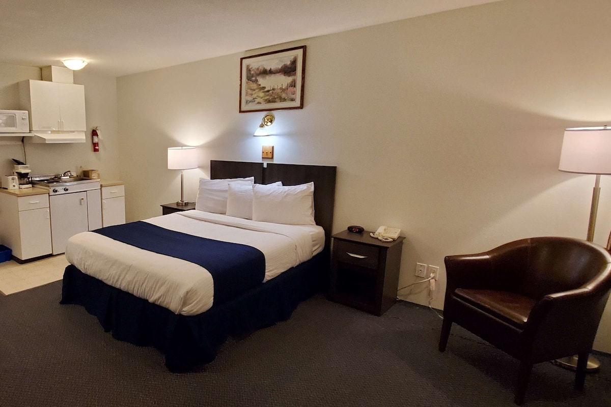 Ein Hotelzimmer mit einem Bett, einem Schreibtisch mit einer Mikrowelle, einem Sessel und einem Bild an der Wand.