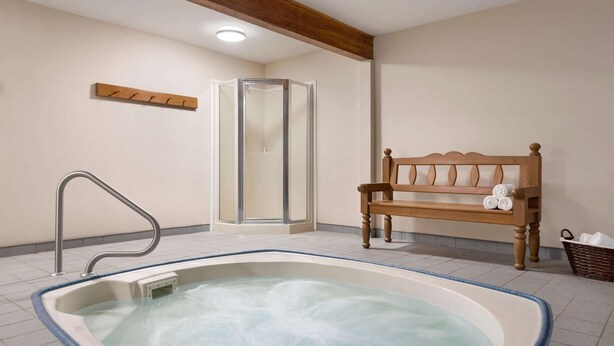 A spa room with a hot tub, a wooden bench, a glass shower enclosure, and a towel rack.