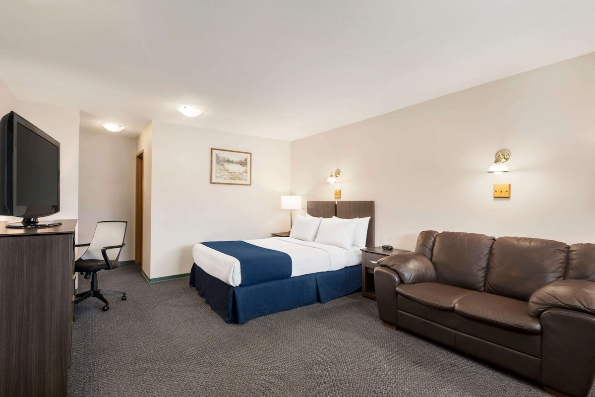 Ein Hotelzimmer mit einem Bett, einem Schreibtisch mit Fernseher, einem Ledersofa und einer Schreibtischlampe.