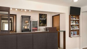 A reception area with a dark wooden reception desk, a refrigerator with beverages, a poster, and a bookshelf with magazines.