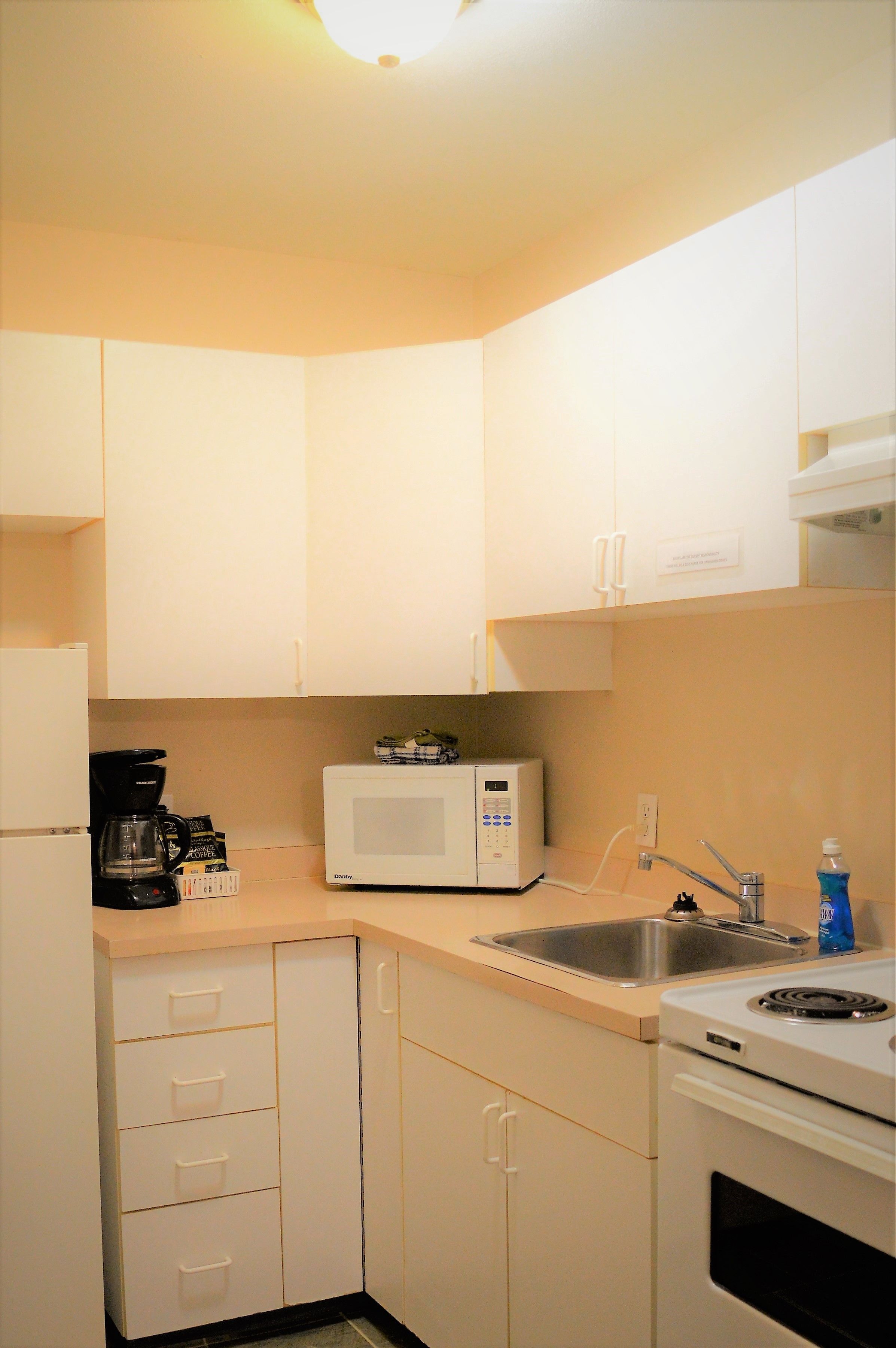 A small kitchenette with white cabinets, a microwave, a coffee maker, a sink, and a stove.