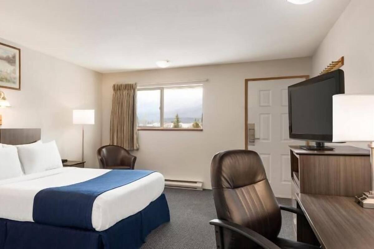 Ein Hotelzimmer mit Bett, Schreibtisch mit Fernseher, Stuhl, Fenster mit Vorhängen und einem Bild an der Wand.