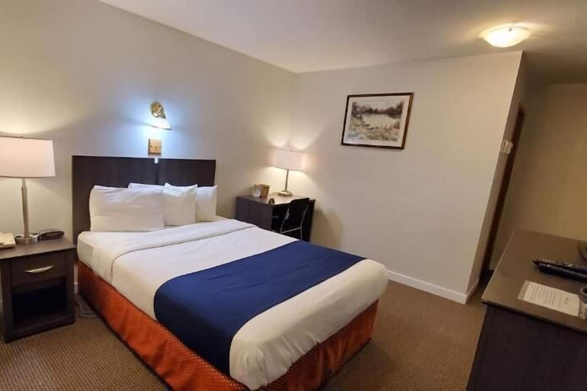 Ein Hotelzimmer mit einem Bett, zwei Nachttischen, einem Schreibtisch, einem Stuhl, einer Lampe und einem Bild an der Wand.