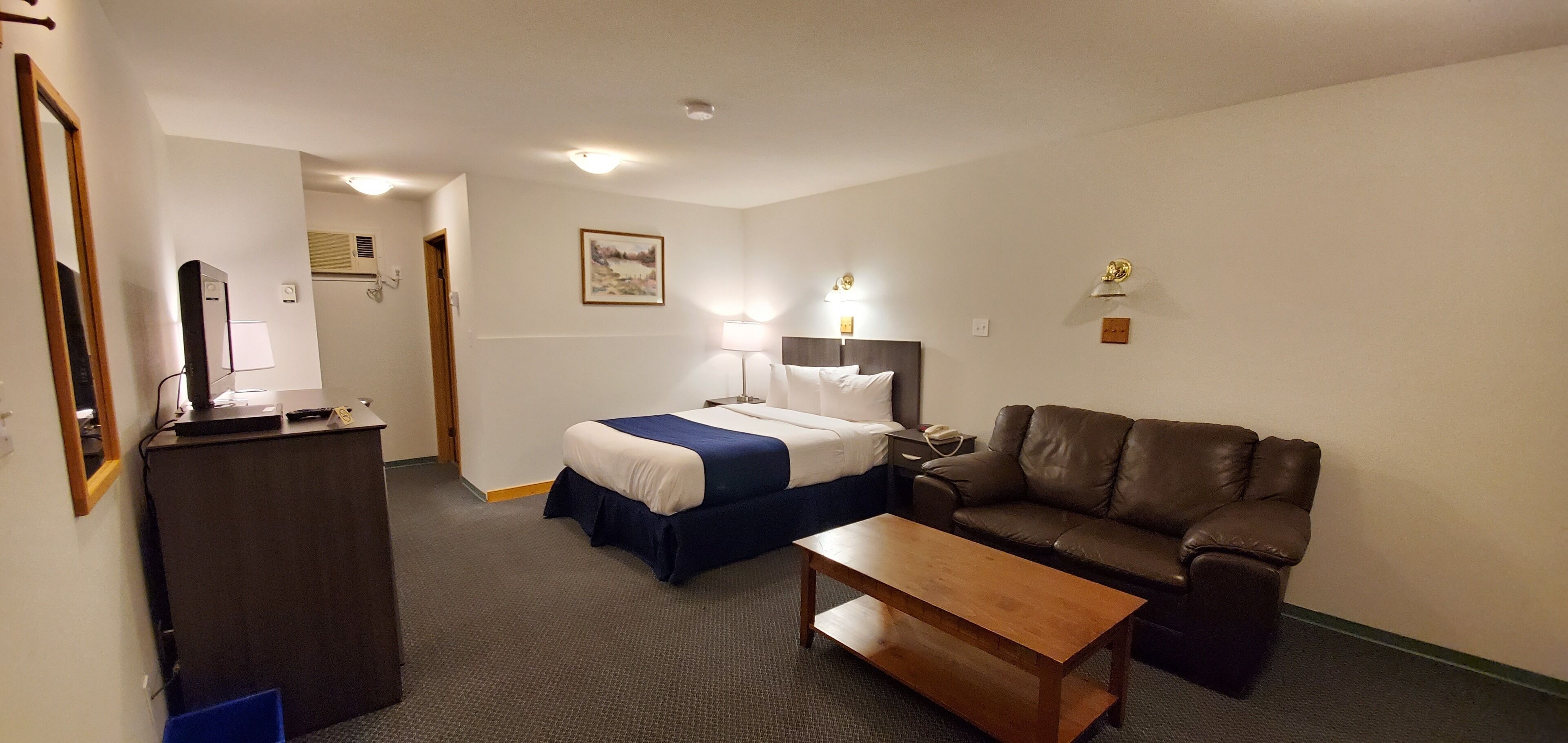 Une chambre d’hôtel avec un lit, un bureau équipé d’un ordinateur, un canapé en cuir marron et une petite table en bois.