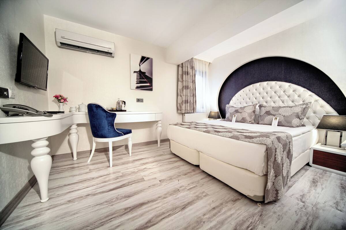 A modern bedroom with a large bed, a desk, a chair, and a television.
