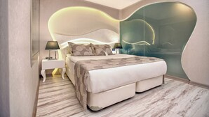 Un dormitorio moderno con una cabecera curvada, una mesita de noche con lámpara, una cama con manta estampada y un espejo grande.