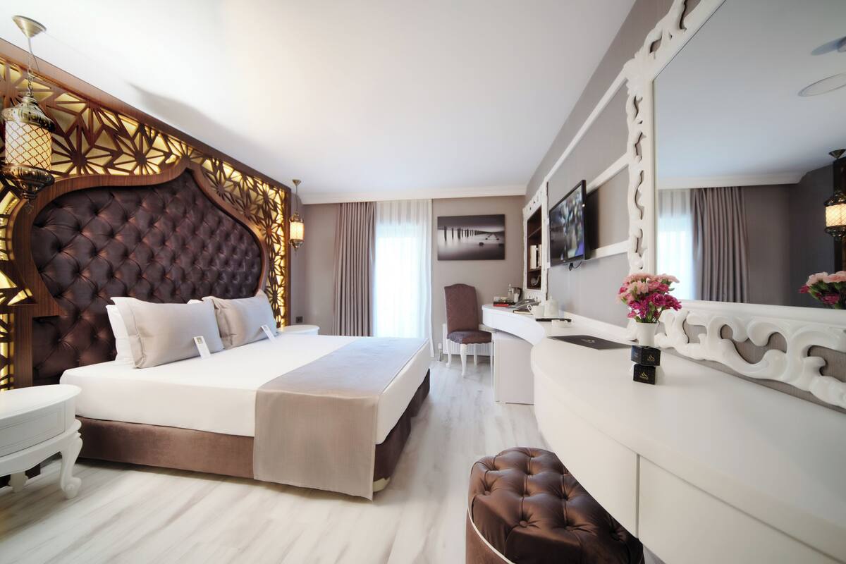 A hotel room with a large bed, a desk, a chair, a vanity, and a mirror.