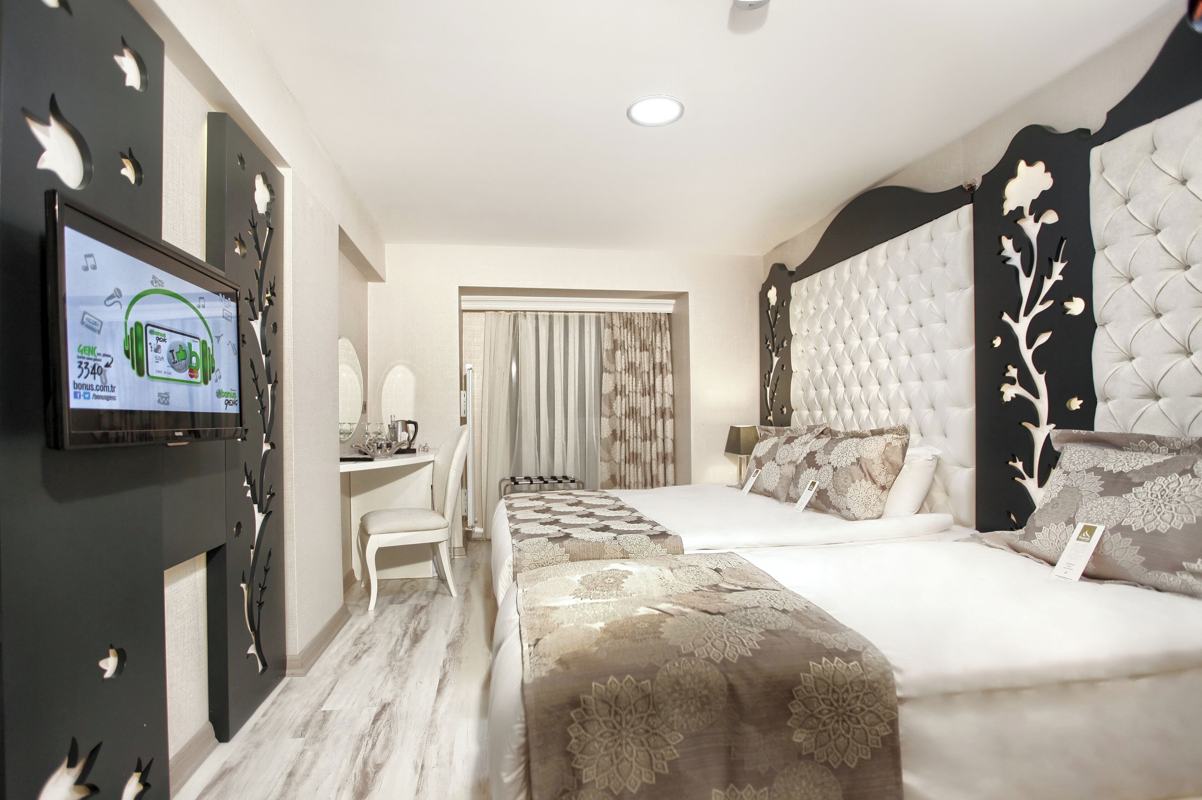 A hotel room with a large bed, a desk with a chair, a television mounted on the wall, and a window with curtains.