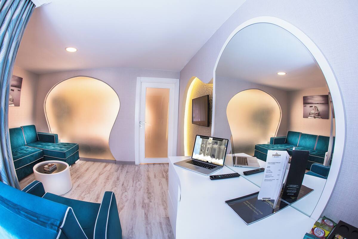 A modern hotel lobby with teal sofas, a white reception desk, and a large mirror reflecting the space.