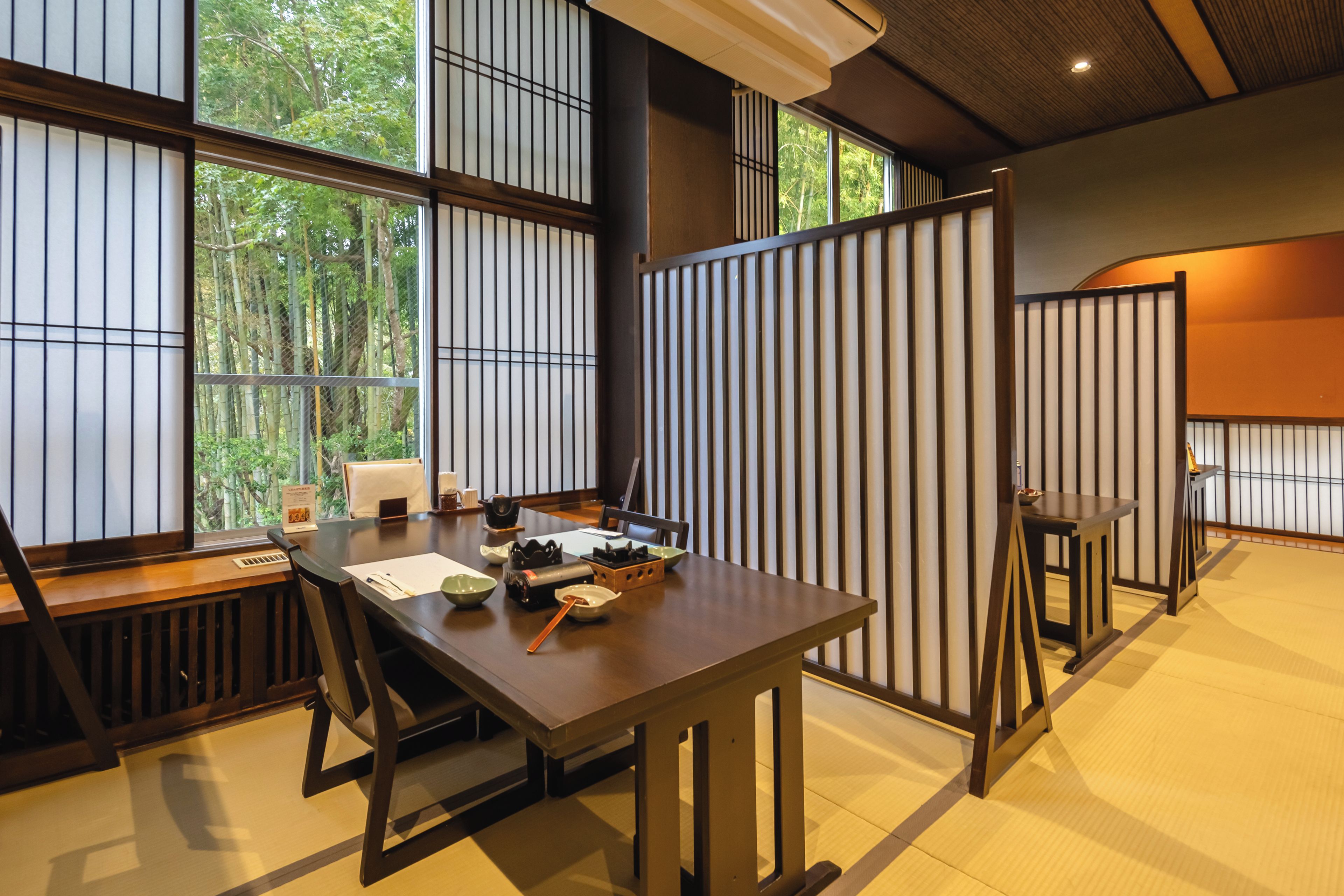 A room with a large window, a wooden table, and a partition with vertical slats.