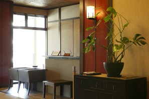 Een traditionele Japanse kamer met tatami vloerbedekking, een lage tafel met stoelen, een potplant en een wandlamp.