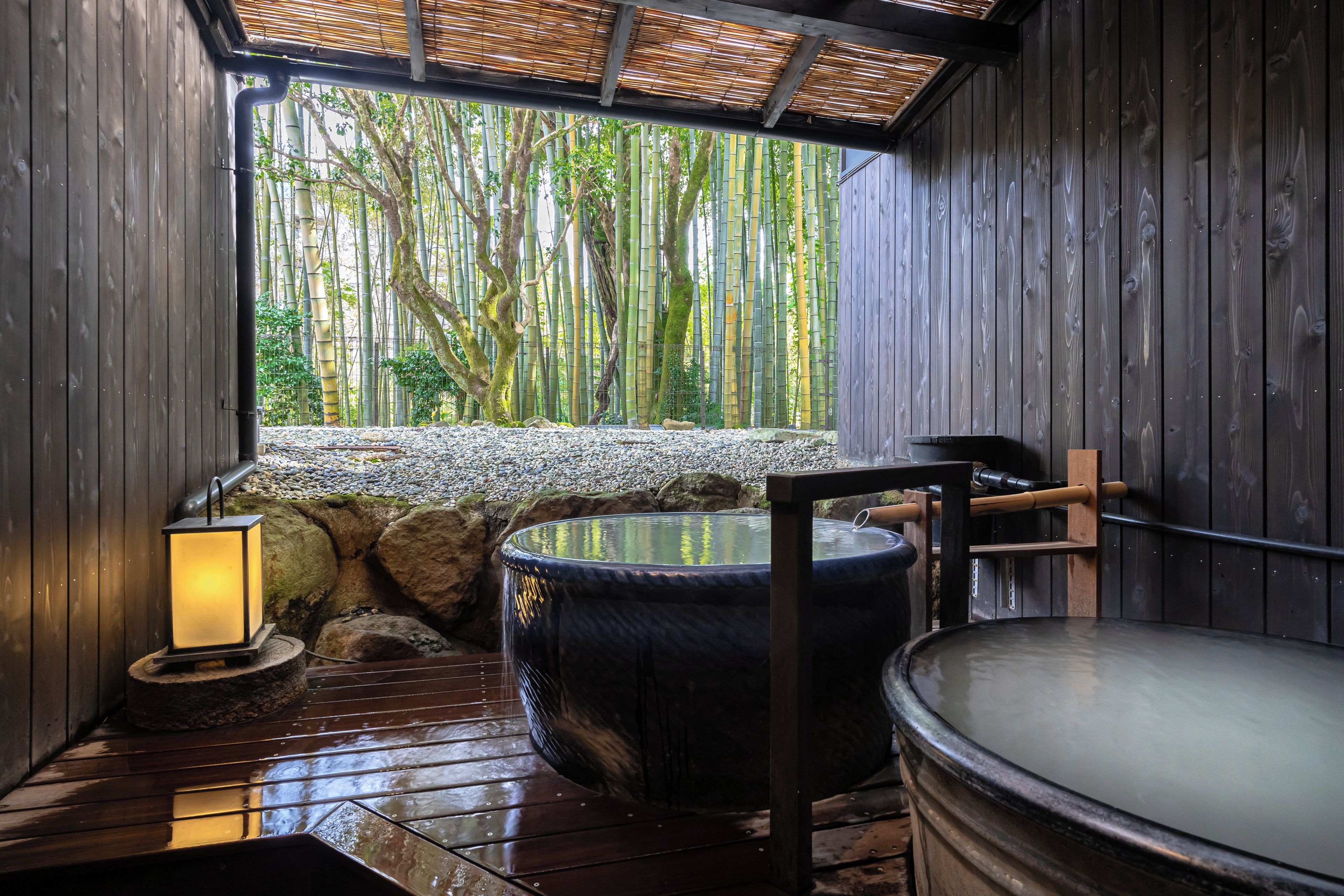 Un espacio de spa de madera con un jacuzzi, una pared de piedra y vistas a un bosque de bambú.