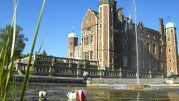 A historic building with a fountain in the foreground, surrounded by water and greenery.