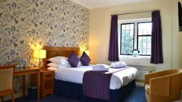 A hotel room with a bed, bedside tables, a chair, a window with curtains, and a patterned wallpaper.