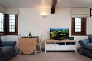A living room with a wooden table, two grey sofas, a TV on a white stand, and a painting of a landscape.