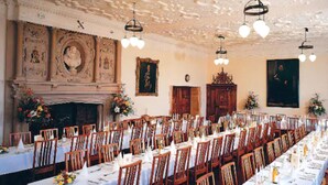 A long dining table set with chairs, a fireplace, and framed artwork on the walls. - Madingley Hall (Cambridge)