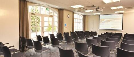A conference room with rows of chairs, a projector screen, and a large window with curtains.