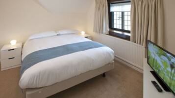 A bedroom with a bed, bedside tables, a TV, and a window with curtains.