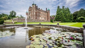 A historic building with a fountain and a pond with lily pads. - Madingley Hall (Cambridge)