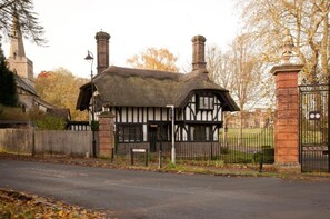 A traditional Tudor-style building with a thatched roof, black and white timber framing, and two chimneys.
