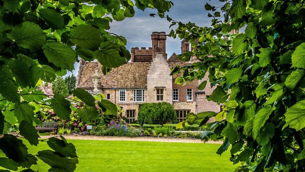 A historic building with a large lawn in front, surrounded by lush greenery. - Madingley Hall (Cambridge)