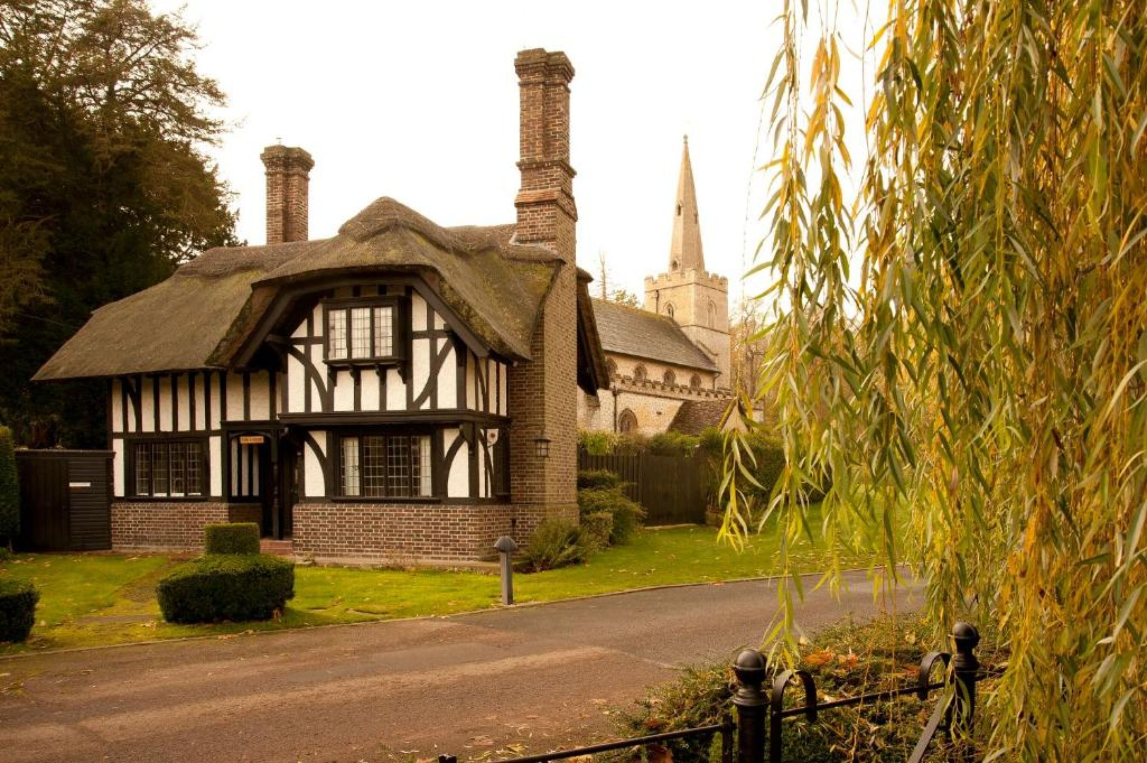 Una casa de estilo Tudor tradicional con techo de paja, chimenea de ladrillo y un pequeño jardín.