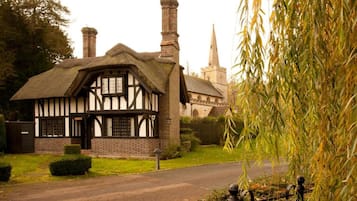 Una casa de estilo Tudor tradicional con techo de paja, chimenea de ladrillo y un pequeño jardín.
