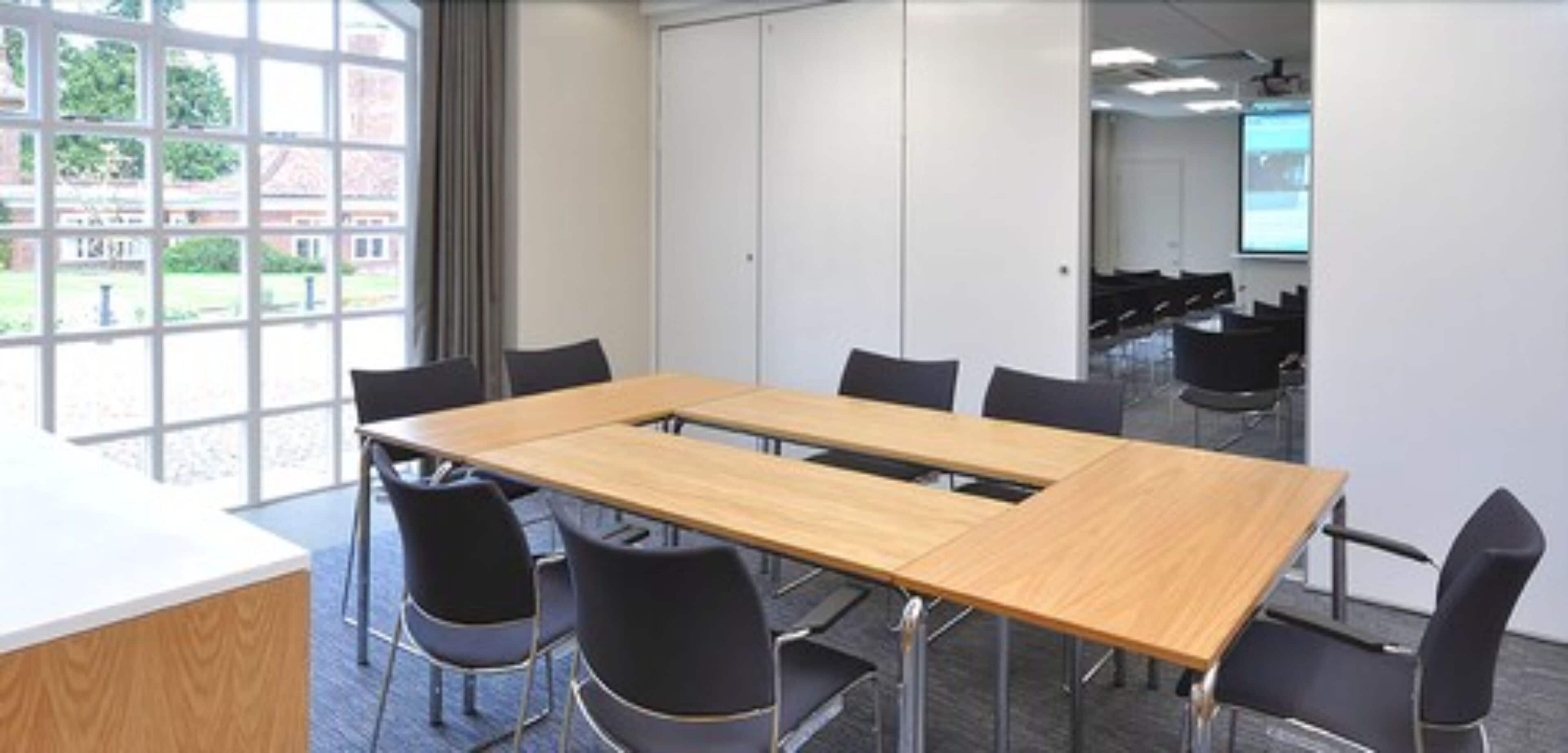 A conference room with a long table, black chairs, a whiteboard, and a projector screen.