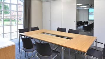 A conference room with a long table, black chairs, a whiteboard, and a projector screen.