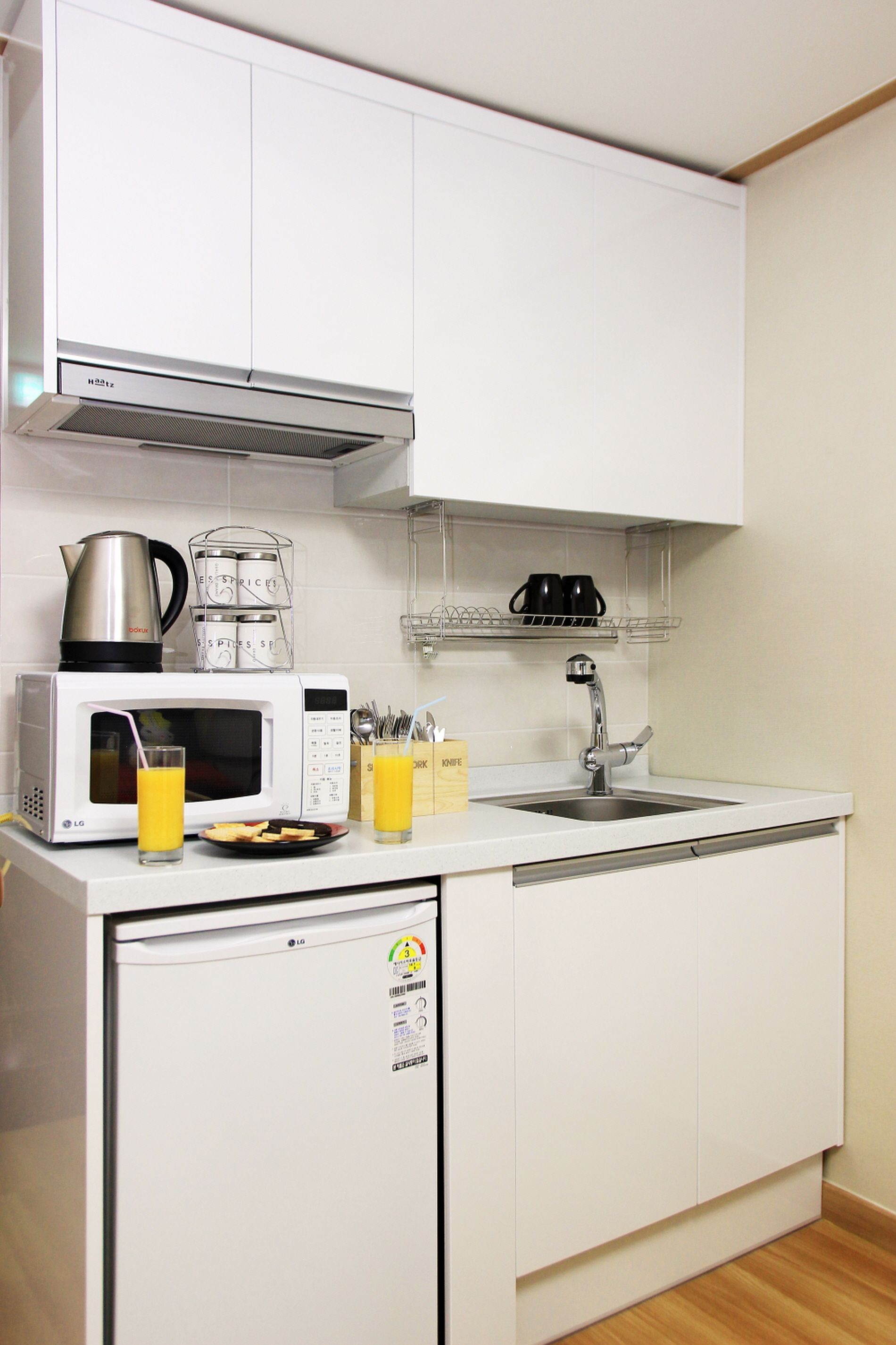A compact kitchen with a microwave, kettle, blender, and a sink.