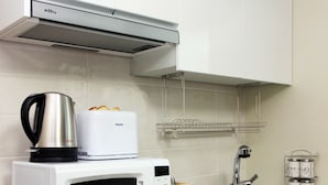 Una cocina con armarios blancos, microondas, hervidor, tostadora, pileta y refrigerador.