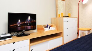 Un dormitorio con televisor, escritorio de madera, cajones, cama, espejo y lámpara roja.