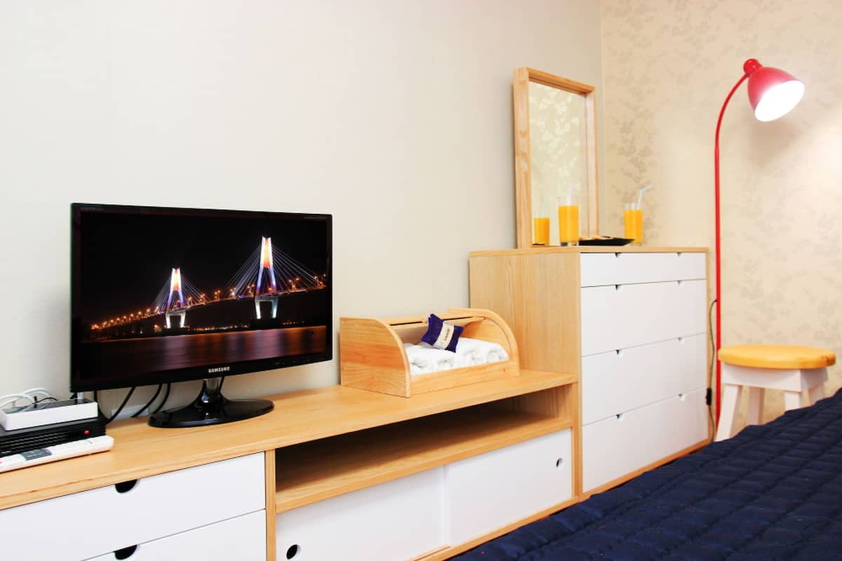 Ein Schlafzimmer mit Fernseher, Holztisch, Schubladen, einem Bett, einem Spiegel und einer roten Lampe.